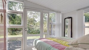A bedroom with a large bed, a mirror, and a sliding glass door leading to a garden.