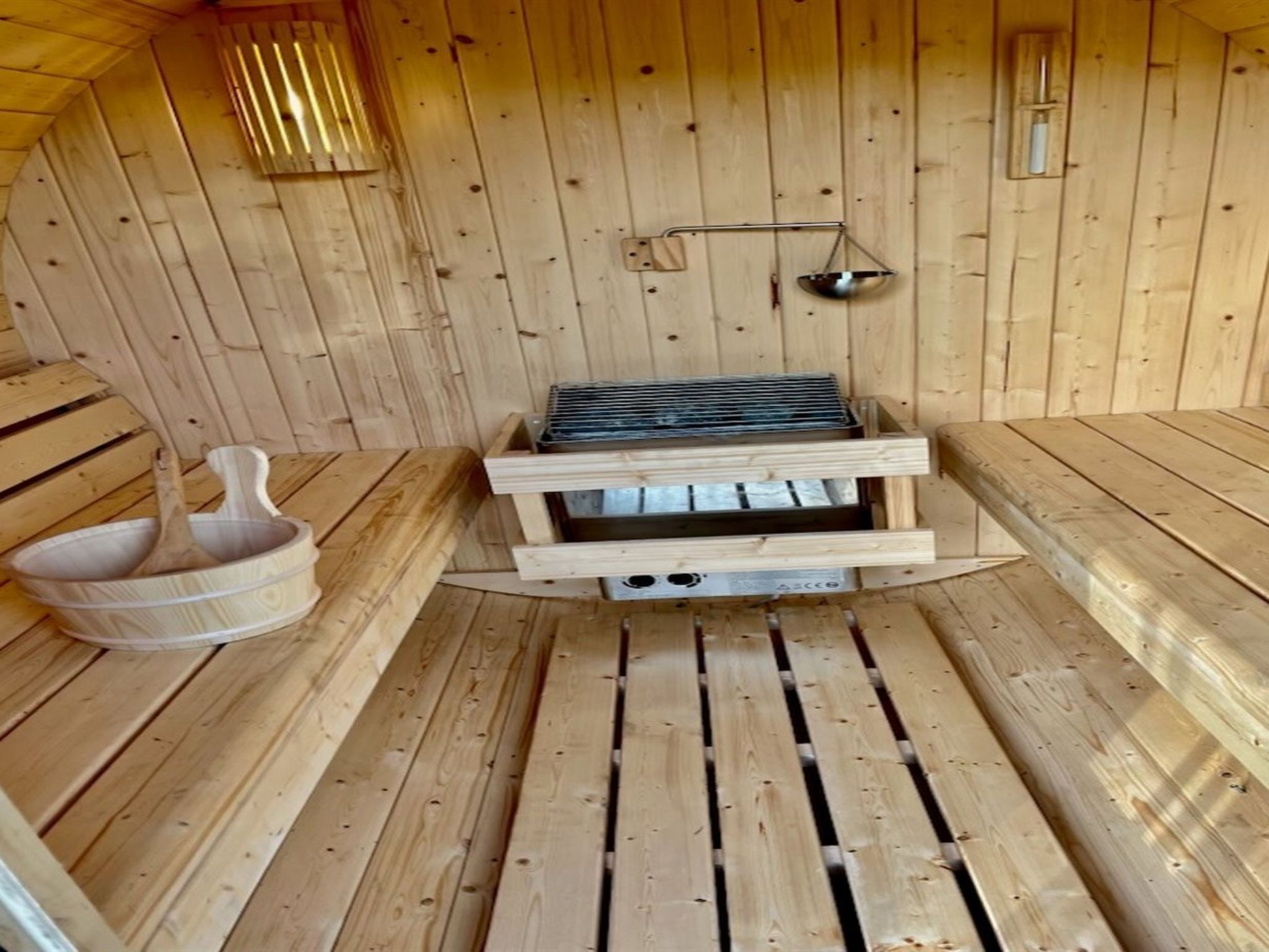 A sauna with wooden walls and benches, a wooden bucket, and a metal grate.