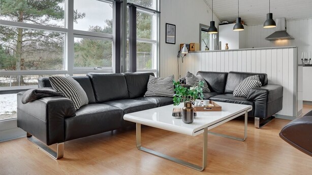 Un salon moderne avec un canapé d’angle en cuir noir, une table basse blanche et des luminaires suspendus.