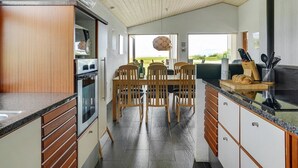 A modern kitchen with wooden cabinets, a dining area with a table and chairs, and a view of the outdoors. - "Roope" - 50m from the sea by Interhome (Storvorde)