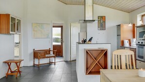 A compact kitchen with modern appliances, a dining area with a wooden table and chairs, and a small seating area with a bench. - "Roope" - 50m from the sea by Interhome (Storvorde)