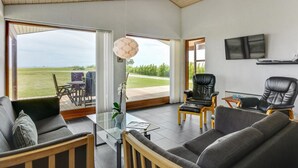 A spacious living room with a large glass door leading to a deck, a comfortable sofa, a coffee table, and a TV mounted on the wall. - "Roope" - 50m from the sea by Interhome (Storvorde)