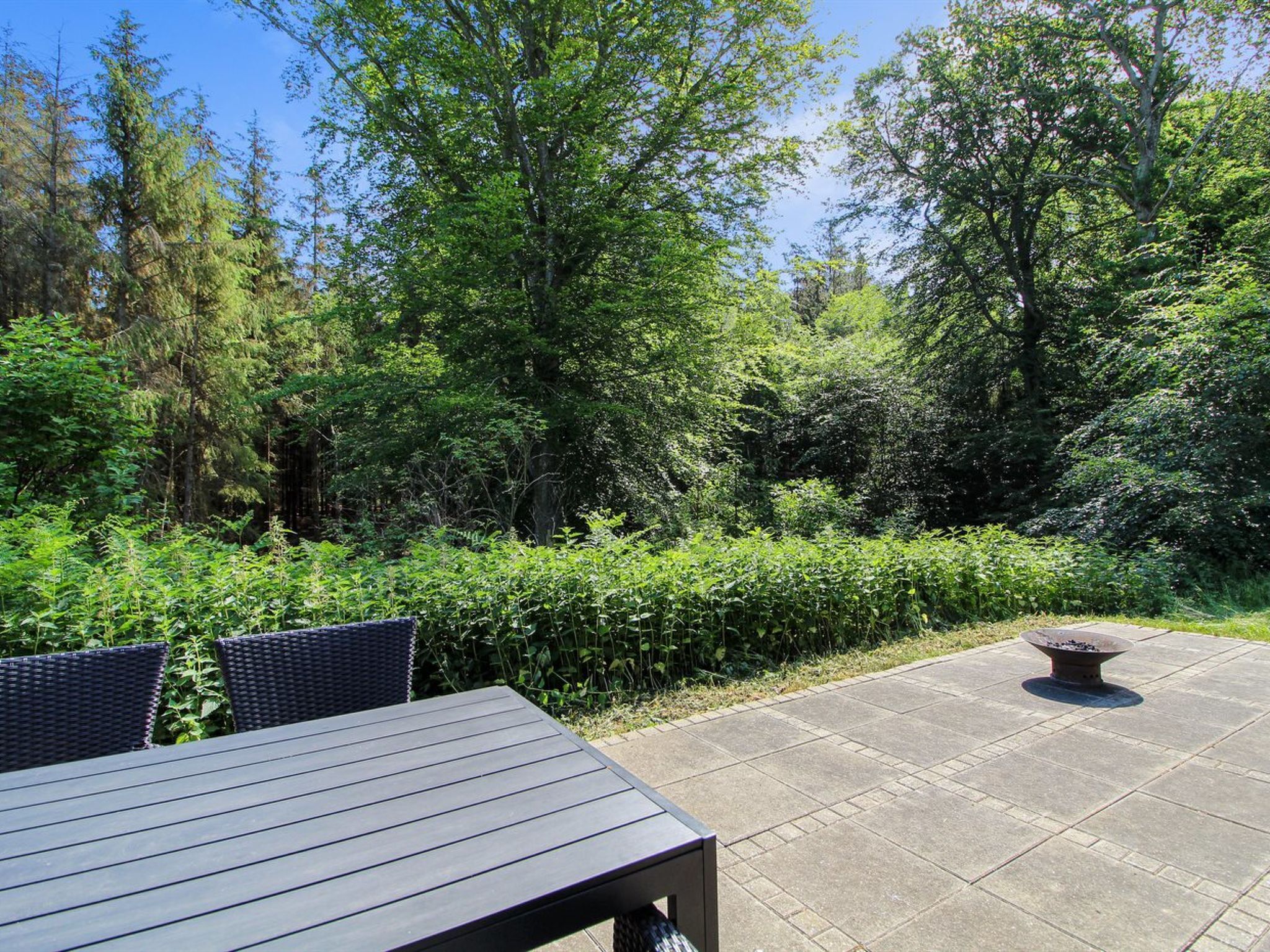 A patio area with a table and chairs, surrounded by lush greenery and trees.