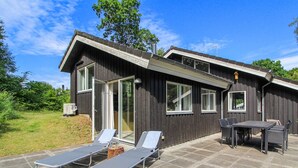 A modern wooden house with a patio area featuring two lounge chairs and a table.