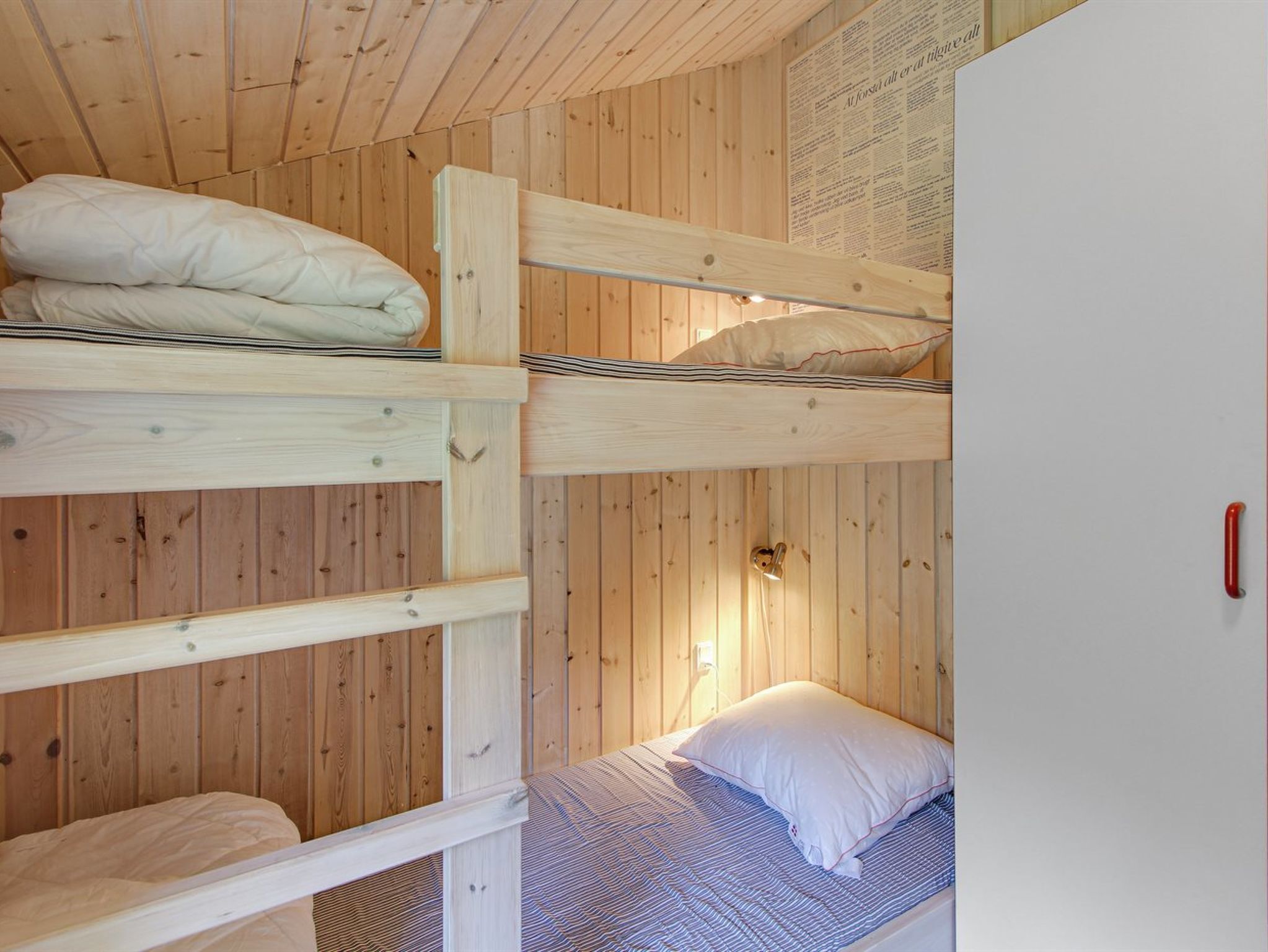 Quarto com beliches de madeira e uma cama simples com cobertor listrado.