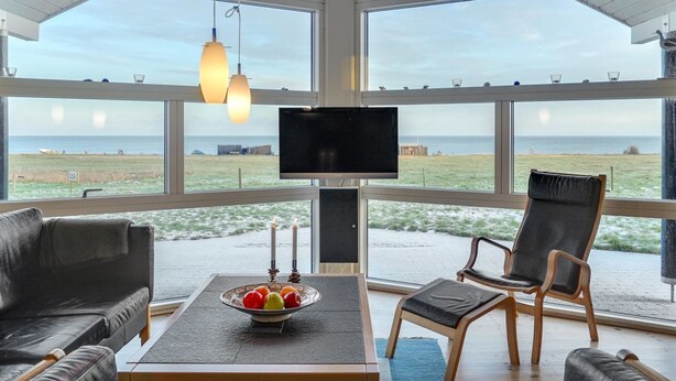 Een ruime kamer met een grote televisie, comfortabele zitmogelijkheden en uitzicht op het strand.