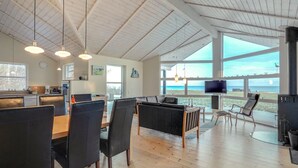 Een ruime woonkamer met een grote eettafel, zachte zithoek, een open haard en uitzicht op de oceaan.