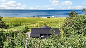 Een huis met een donker dak, omringd door weelderige begroeiing en uitzicht op zee.