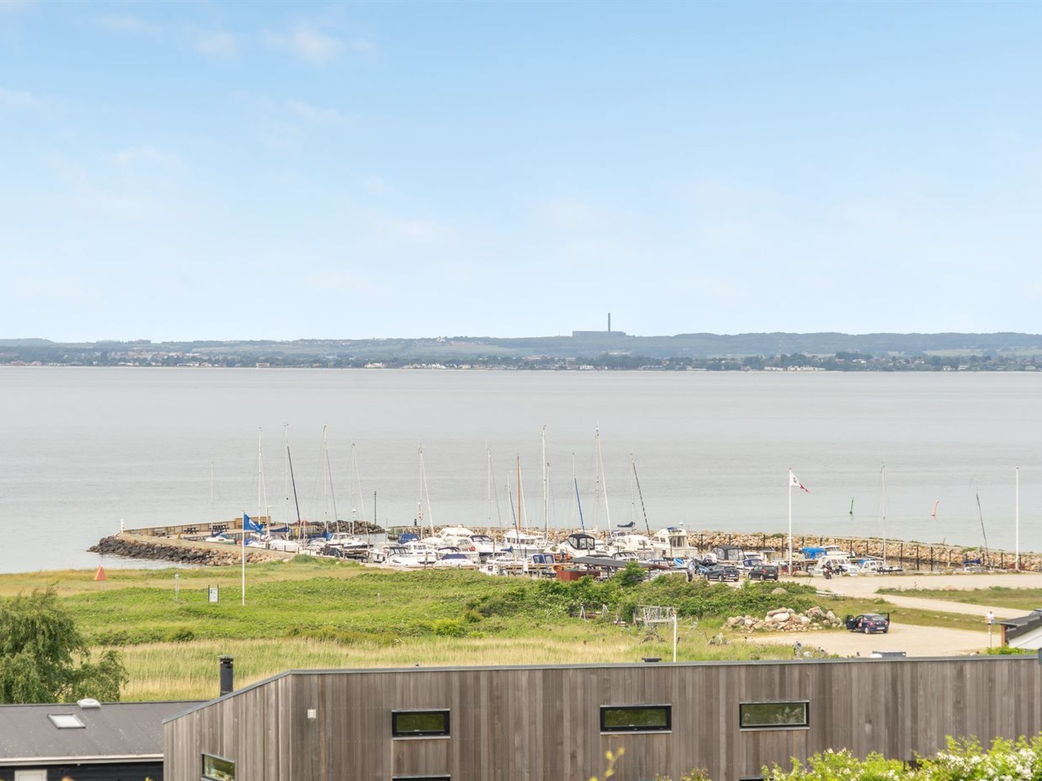 A marina with boats docked, a distant industrial structure, and a grassy area in the foreground.