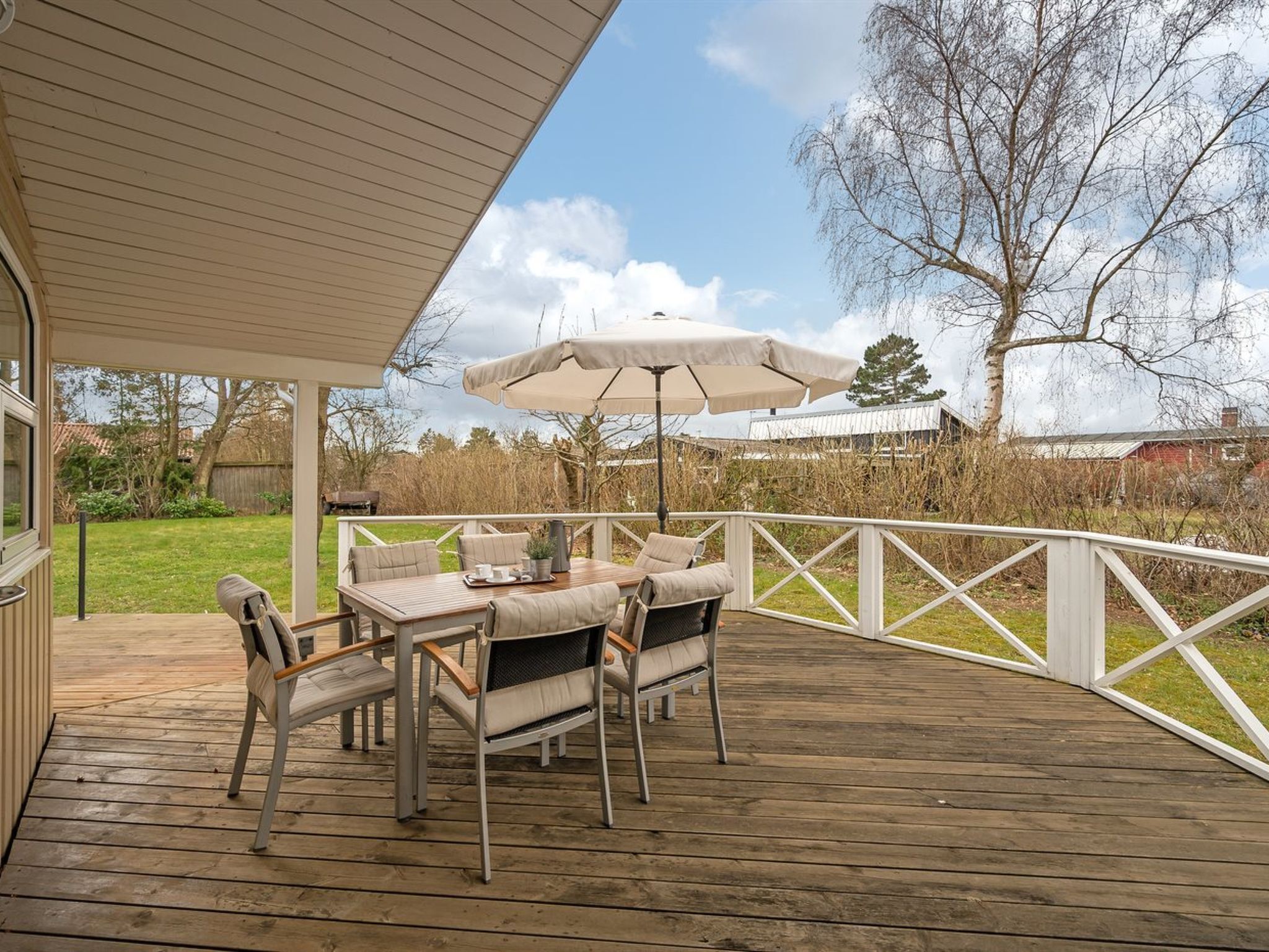 Une terrasse couverte avec une plateforme en bois, du mobilier d’extérieur et un parasol blanc.