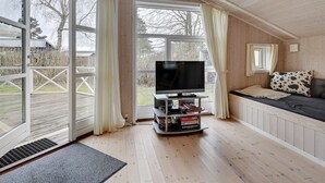 Een gezellige kamer met een grote televisie op een standaard, houten vloeren en een bank met een kussen met patroon.