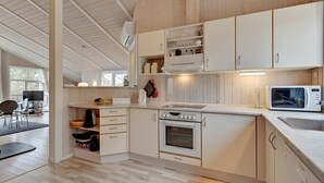 Een moderne keuken met witte kasten, een inbouwoven, magnetron en een groot raam dat voor natuurlijk licht zorgt.