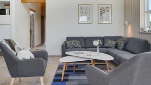 A modern living room with a grey sofa, two armchairs, a coffee table, and two framed botanical prints on the wall.