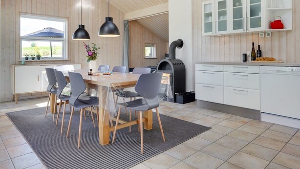 A modern kitchen with a wood-paneled ceiling, a central island with chairs, and a built-in stove.