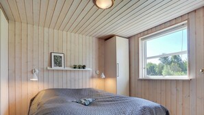 A bedroom with a large bed, wooden walls, a window, and a shelf with plants.