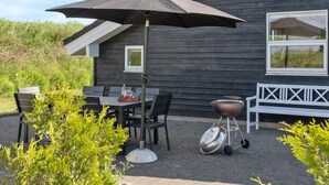An outdoor patio with a table and chairs, a barbecue grill, and a white bench.