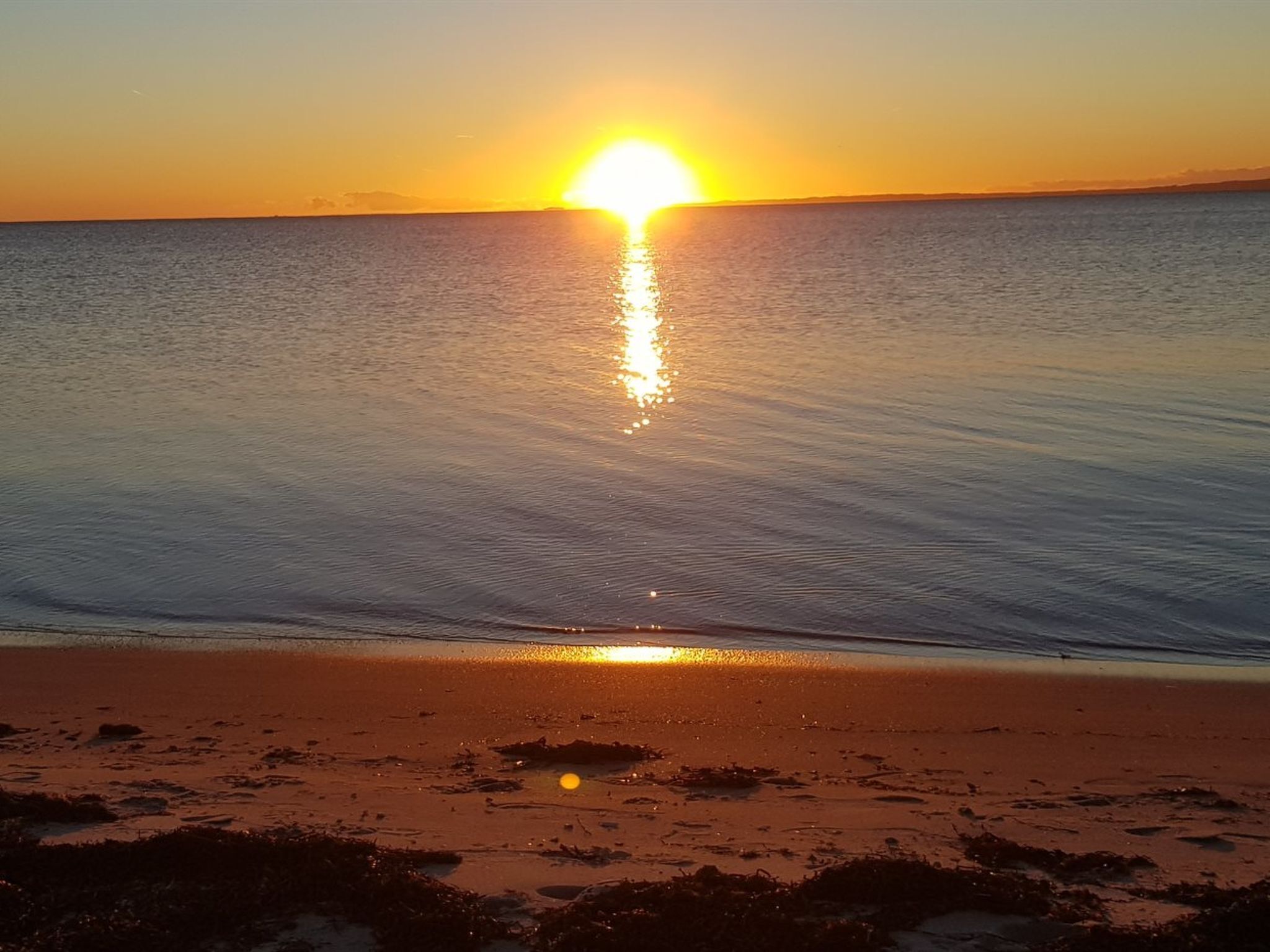 Auringonlasku tyynen meren yllä, edessä hiekkaranta.