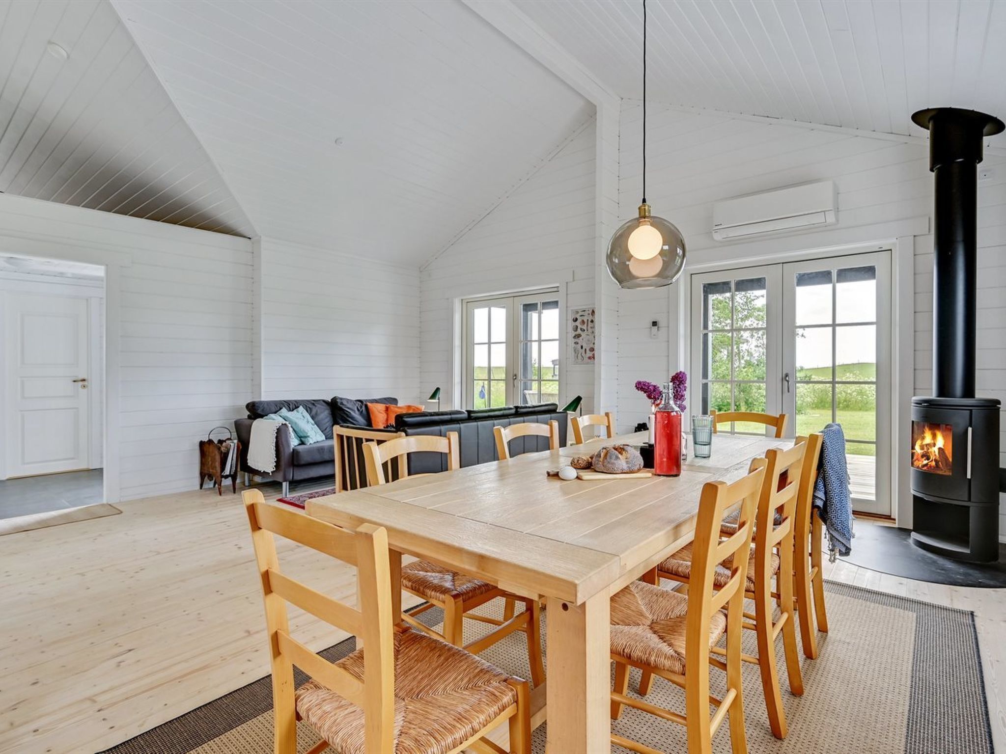 A spacious room with a large dining table, wooden chairs, a sofa, and a wood-burning stove.