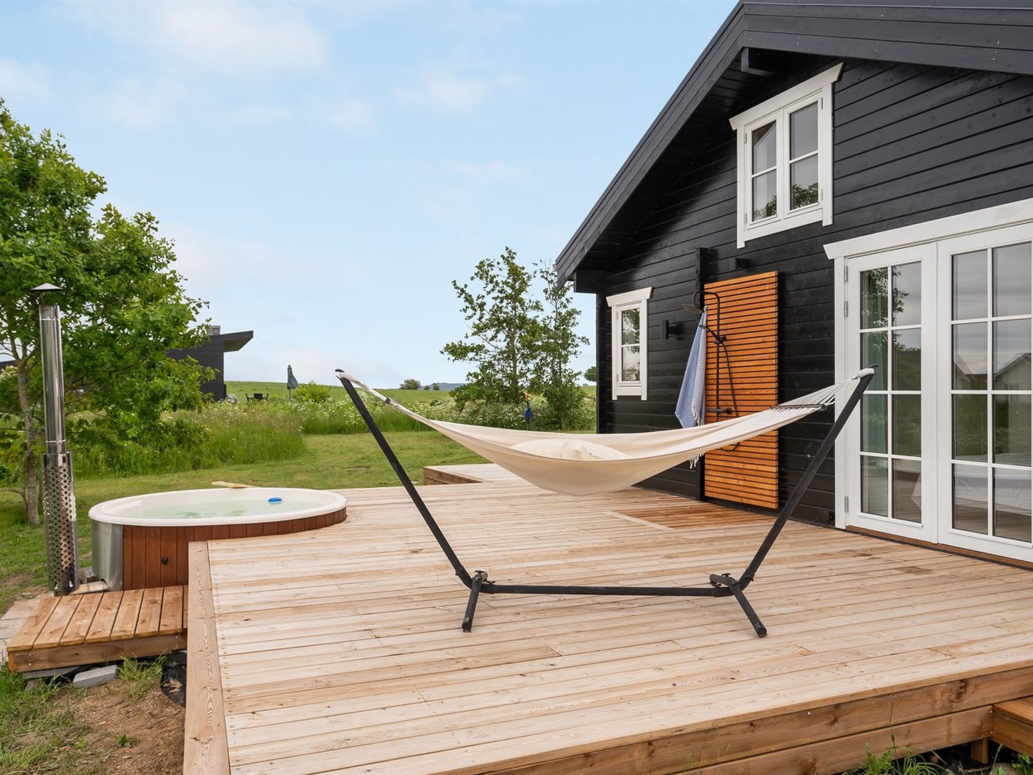 A wooden deck with a hammock, a hot tub, and a sauna.