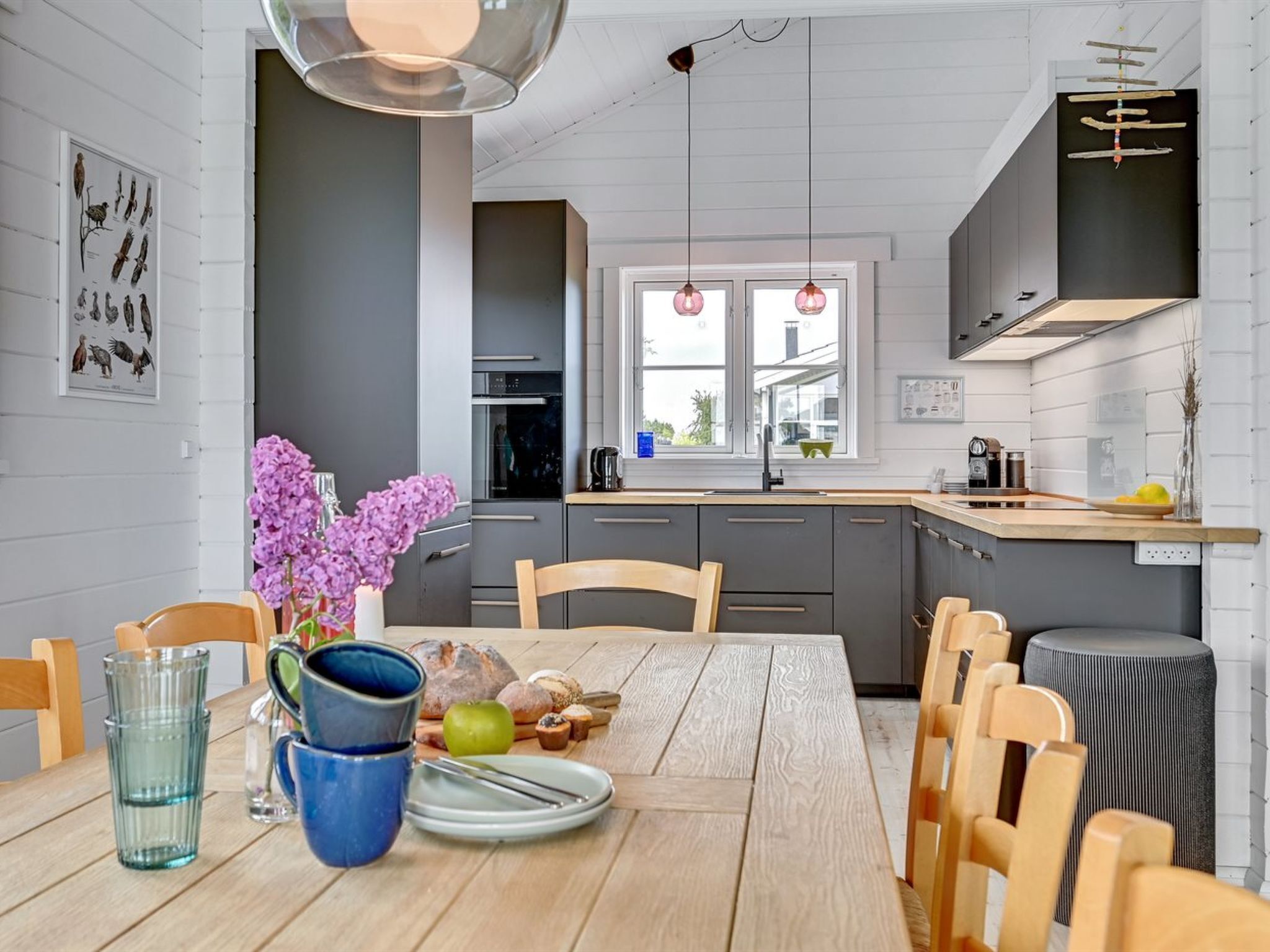 A modern kitchen with grey cabinets, a wooden dining table, and a window with a view.