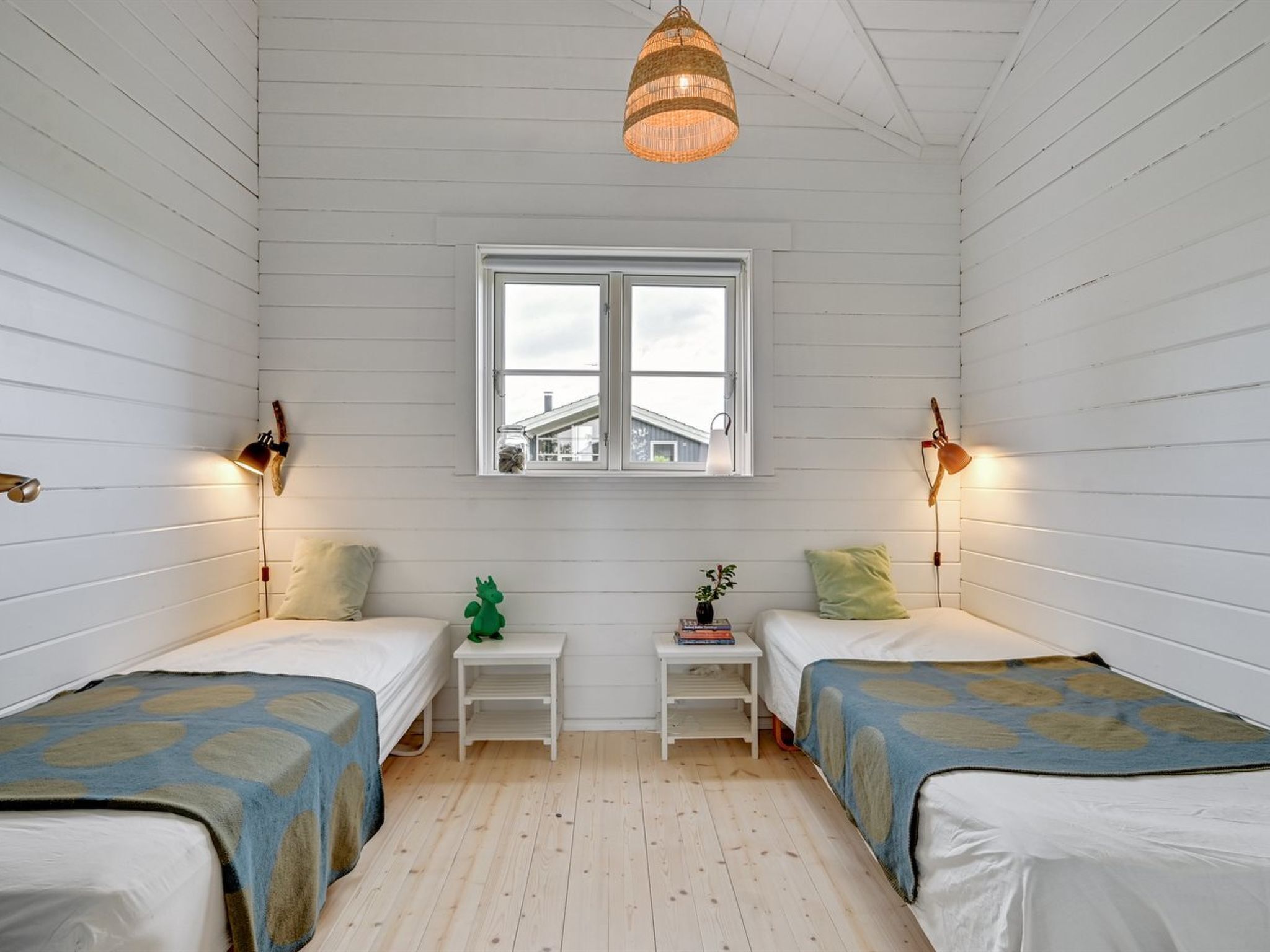 A room with two beds, a window, and a hanging light fixture.