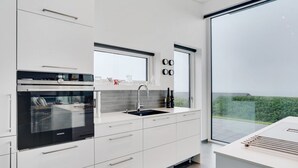 Una cocina moderna con armarios blancos, horno integrado y un amplio ventanal con vistas al exterior.
