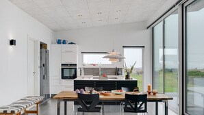 Una cocina moderna con una isla grande, armarios blancos y una zona de comedor con un banco y sillas.