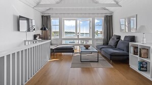 Ein modernes Wohnzimmer mit Holzboden, einem grauen Sofa, einem Couchtisch und einem Bücherregal.