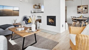 Un salon moderne avec une cheminée, un coin repas avec des chaises en osier et un grand tableau accroché au mur.