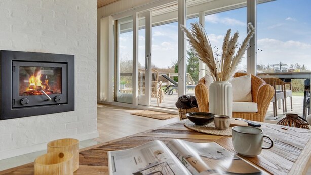 Un salon moderne doté d’une cheminée, de grandes fenêtres et d’une table en bois sur laquelle sont posés des magazines.