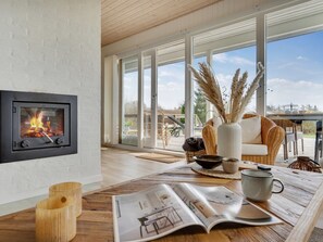 A modern living room with a fireplace, large windows, and a wooden table with magazines. - "Stygge" - 400m from the sea by Interhome (Ebeltoft)