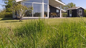 Een modern huis met een groot raam, een overdekt terras en een klein bijgebouw.