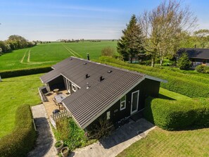 A modern house with a sloped roof, a patio with outdoor furniture, and a well-maintained garden.