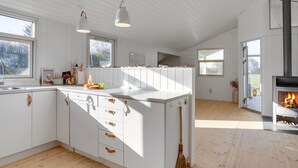 Een moderne keuken met witte kasten, een centraal eiland met lades, hanglampen en een houtgestookte kachel.