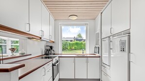 A modern kitchen with white cabinets, a wooden countertop, a built-in oven, a microwave, and a refrigerator. There is a window providing a view of the outdoors. - "Teija" - 300m from the sea by Interhome (Odder)