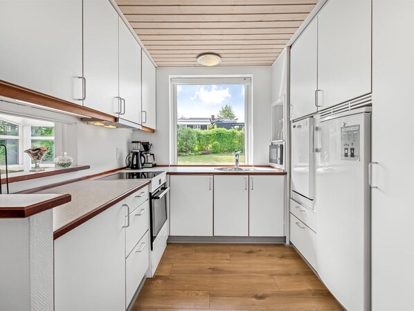A modern kitchen with white cabinets, a wooden countertop, a built-in oven, a microwave, and a refrigerator. There is a window providing a view of the outdoors.
