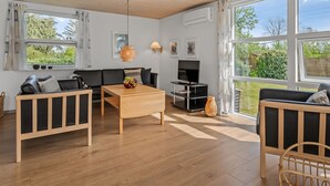 A modern living room with a wooden floor, a sofa, a coffee table, a TV, and large windows offering a view of the outdoors. - "Teija" - 300m from the sea by Interhome (Odder)