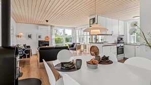 A modern kitchen with white cabinets, a large island, and a dining area with white chairs. - "Teija" - 300m from the sea by Interhome (Odder)