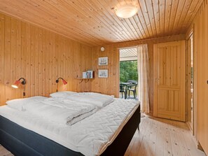 Ein schlicht eingerichtetes Schlafzimmer mit Holzwänden, einem Bett, zwei Wandlampen und einer Tür zu einem Außenbereich.