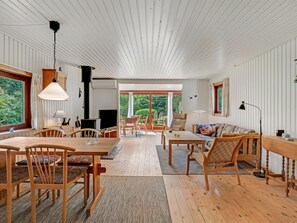 Ein geräumiges Zimmer mit hoher Decke, Holzboden, einer Essecke mit Stühlen und Tisch, einer Couch und einem Fernseher.