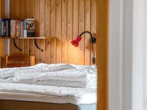 Ein Schlafzimmer mit einer Holzwand, einem Bücherregal, einer roten Schreibtischlampe und einem Bett mit weißer Bettwäsche.