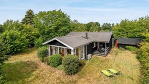 Ein eingeschossiges Haus mit überdachter Veranda, umgeben von dichtem Grün und Bäumen.