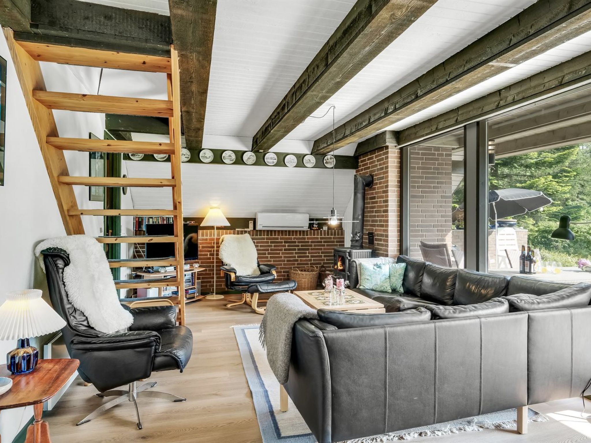Una sala de estar acogedora con una escalera de madera, chimenea, sofá de cuero y comedor con vista al exterior.