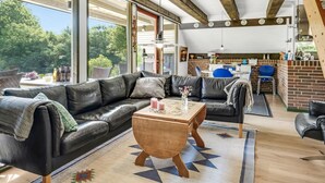 Un vaste espace de vie comprenant un canapé en cuir noir, une table basse en bois et un coin repas avec un mur en briques et des chaises bleues.