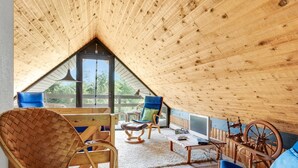 Une pièce mansardée chaleureuse avec des poutres apparentes, une grande fenêtre et une table en bois rustique.