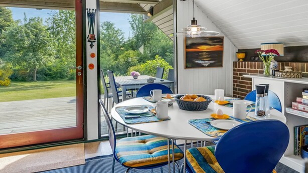 Un coin repas avec une table dressée pour quatre personnes, un panier de pain et une vue sur un jardin, visible à travers une porte vitrée.