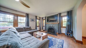 A modern living room with a sectional sofa, a fireplace, and large windows. - Central Erie Vacation Rental ~ 2 Mi to Beach! (Erie)