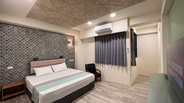A modern bedroom with a large bed, a headboard, an air conditioning unit, a window with curtains, and a television on a stand. - morning travel (Lugu)