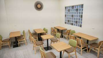 A classroom with wooden tables and chairs, a clock on the wall, and a window with a grid pattern.