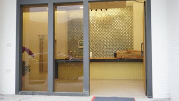 A reception area with a glass door, a wooden reception desk, and a textured wall with a scale-like pattern.